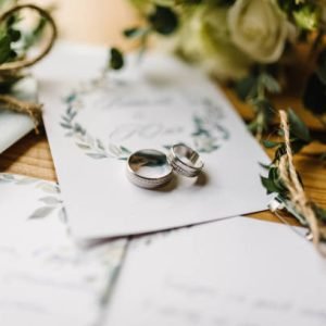 Stylish rings, flowers on wooden table background. Letters from the bride and groom. Vows. Engagement. Luxury marriage and wedding accessory concept.